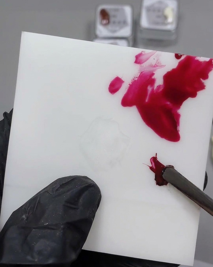 Una herramienta de metal mezclando gel negro en una porción de gel rojo sobre una paleta blanca.