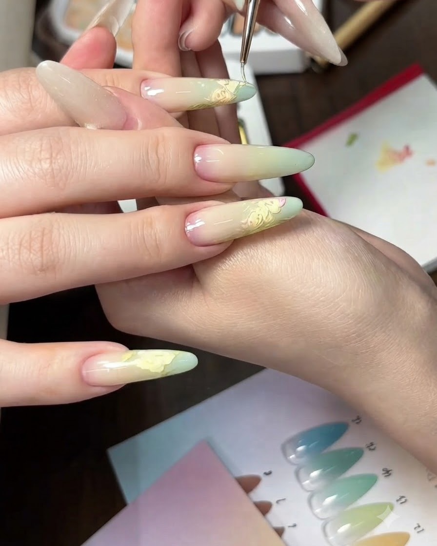 Vista de cerca de la aplicación de un degradado de gel verde claro en las puntas de uñas ovaladas usando una esponja.