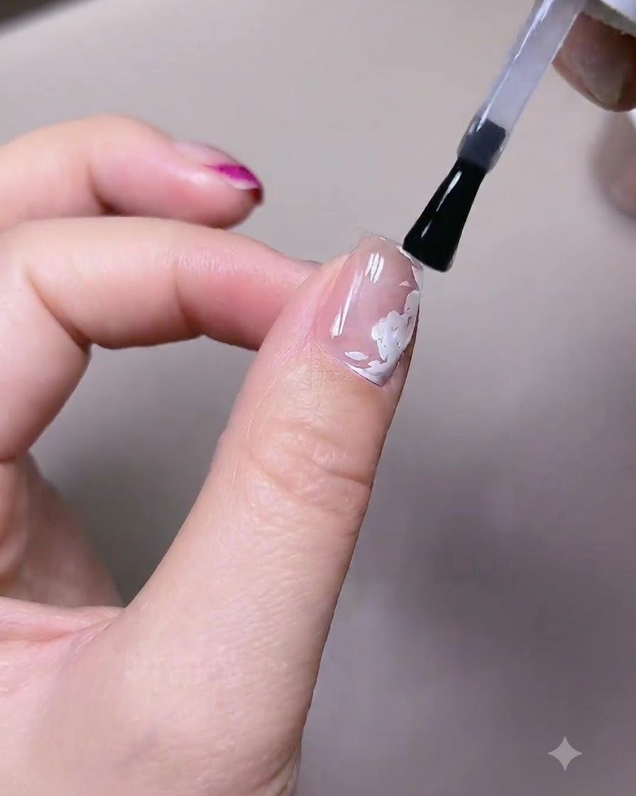 Un pincel aplicando una capa de esmalte en gel superior mate sobre una uña con elementos de rosas blancas pintadas previamente.