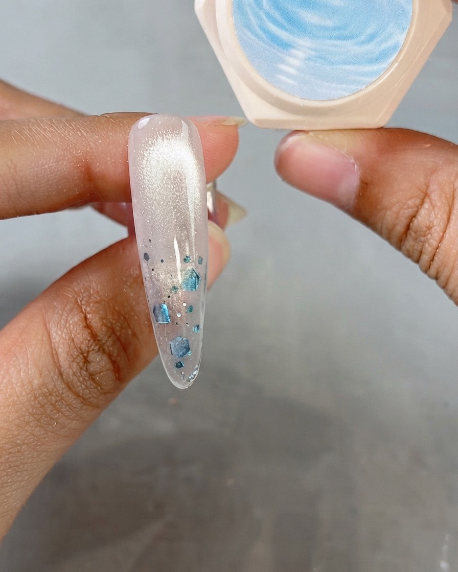 Una uña en almendra que muestra un acabado brillante de ojo de gato con un frasco de gel de cristal al fondo.