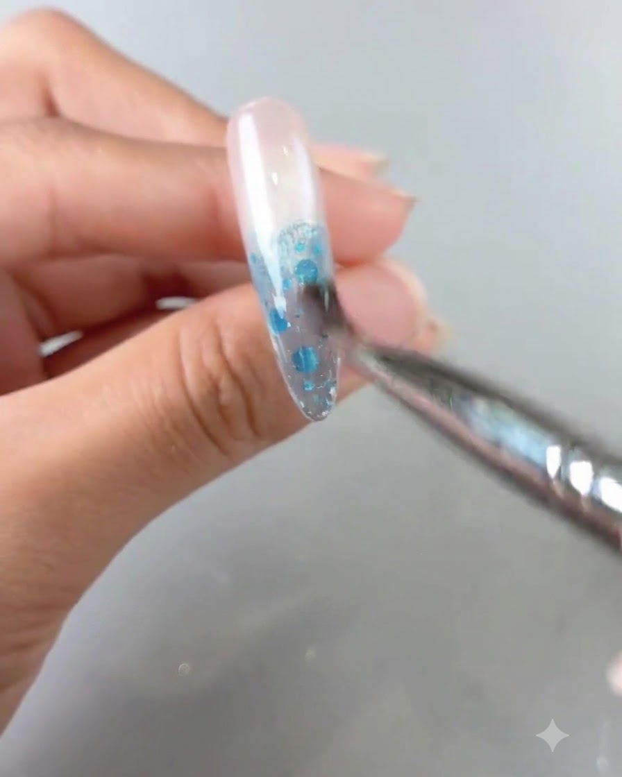 Una vista de primer plano de un pincel difuminando producto de gel azul en una uña para crear un degradado ombré.
