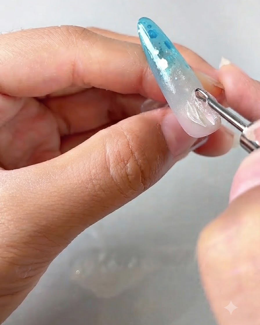 Una herramienta de detalle colocando y levantando los bordes de un pétalo de gel transparente sobre una uña decorada.
