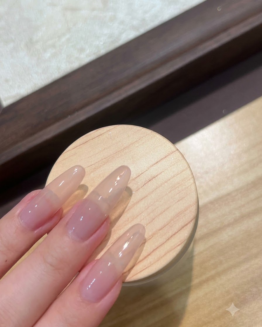 Vista de cerca de uñas postizas largas en tono nude preparándose con una capa de gel base transparente.