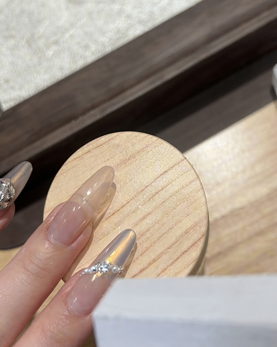 Un técnico de uñas colocando un dije de mariposa blanca escarchada sobre una uña brillante.