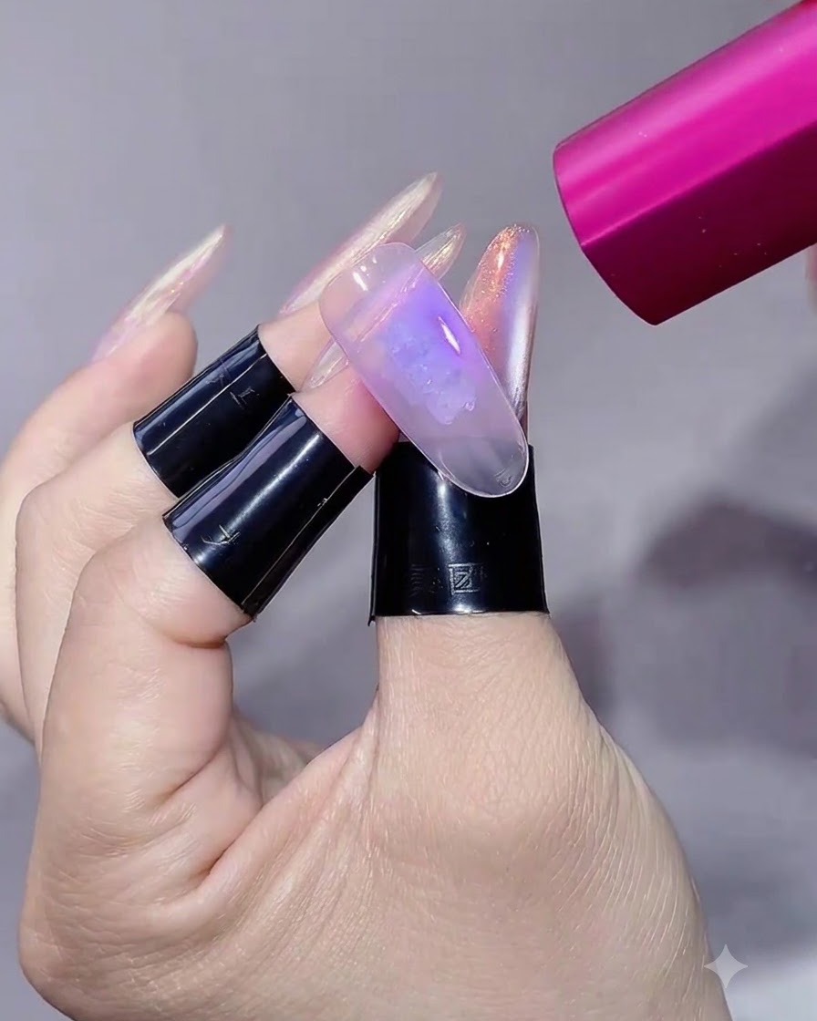 Una lámpara UV/LED rosa de mano proyectando luz sobre una uña esculpida y manicurada.