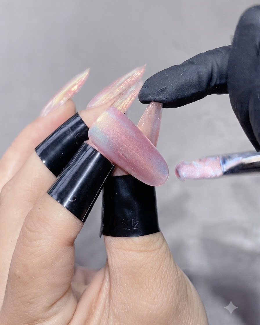 Un pincel de uñas aplicando un gel ojo de gato brillante sobre una uña alargada.