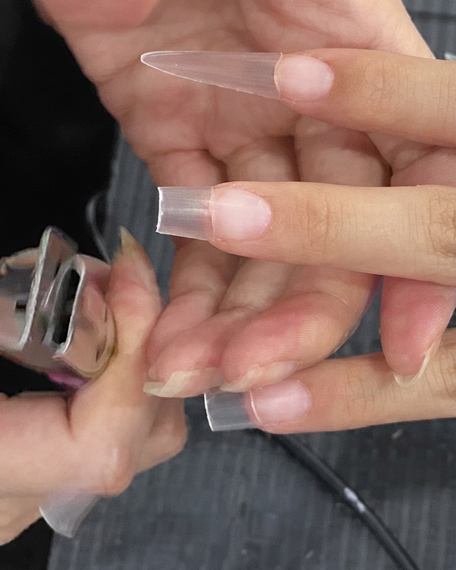 Un cortador de tips para uñas recortando el exceso de longitud de una extensión de uña artificial transparente.