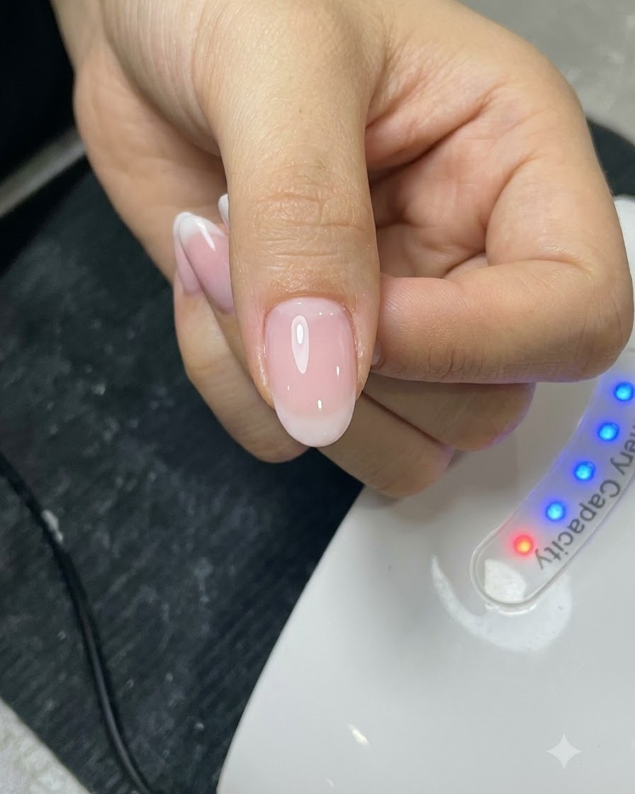 Un pincel aplicando una capa de top coat sobre una uña arreglada frente a una lámpara UV.