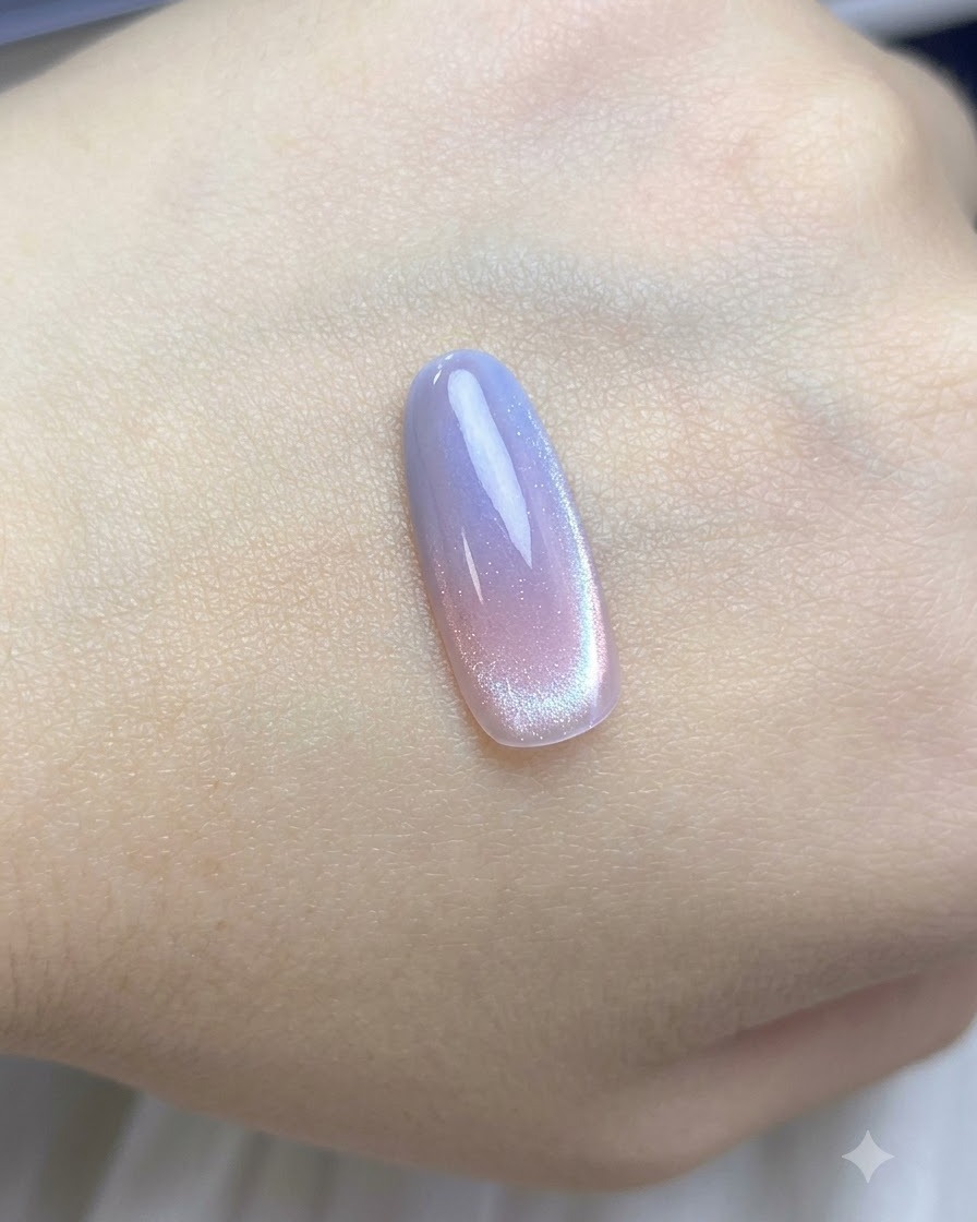 Un pincel aplicando una capa de esmalte cat-eye nude traslúcido sobre la punta de la uña con degradado.