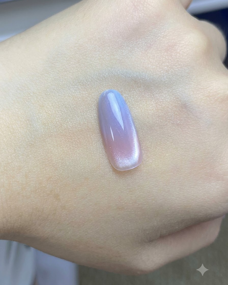 Un pincel aplicando una capa superior brillante final sobre el diseño de uñas cat-eye rosa y azul completado.