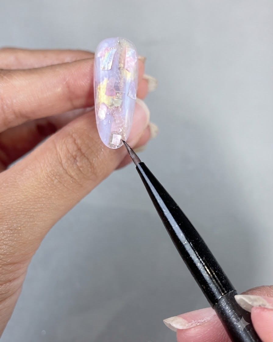 Una mano colocada bajo una lámpara de uñas UV LED curando las piezas de concha aplicadas y el gel constructor.
