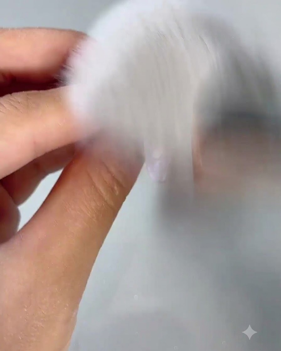 Un pincel de polvo blanco esponjoso barriendo el polvo de uñas de una uña recién pulida.