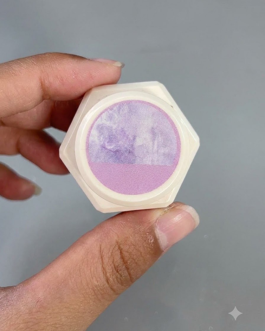 Un envase blanco hexagonal con una pegatina de patrón de acuarela morada en la tapa, sostenido por los dedos.