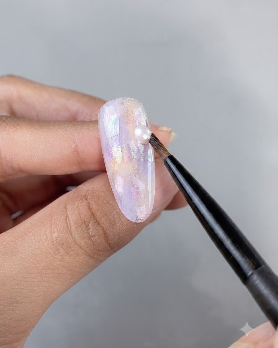 Un pincel artístico fino aplicando una gota de gel brillante sobre una superficie de uña ornamentada e incrustada con conchas.