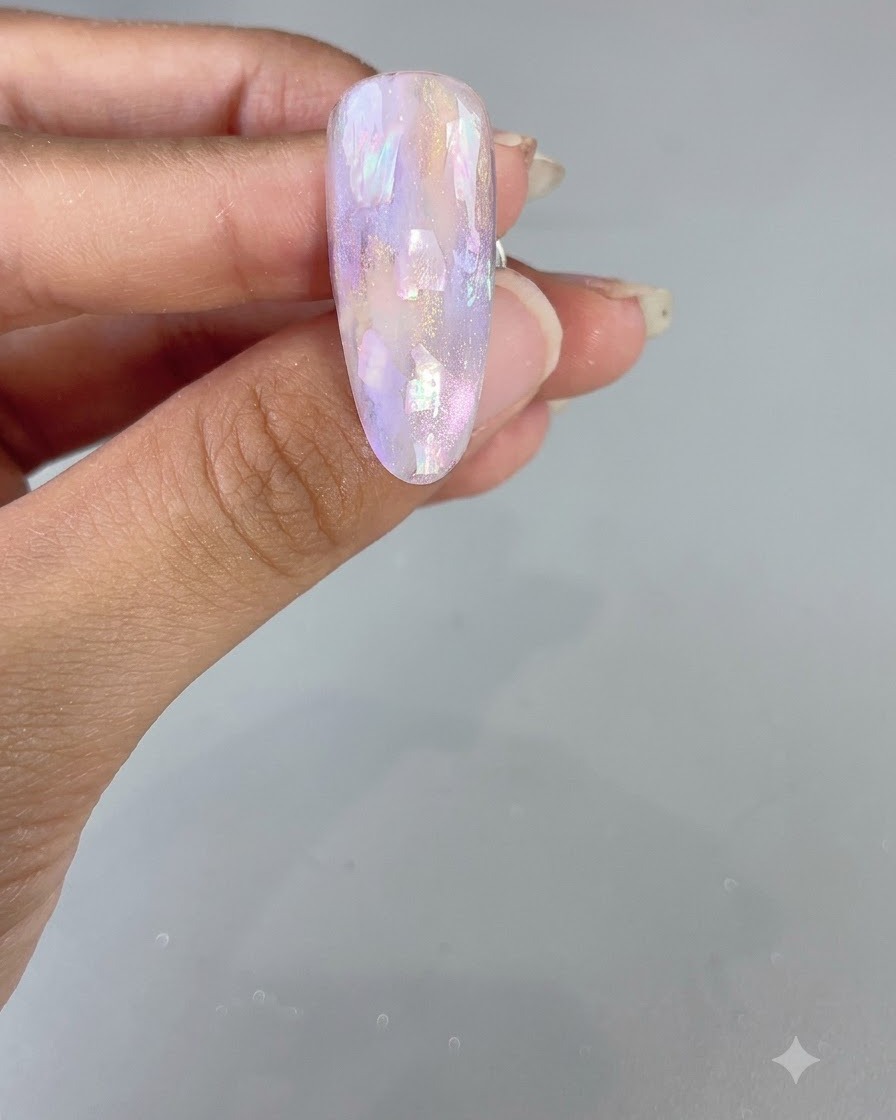 Una uña almendrada terminada con un diseño brillante de acuarela morada y concha.