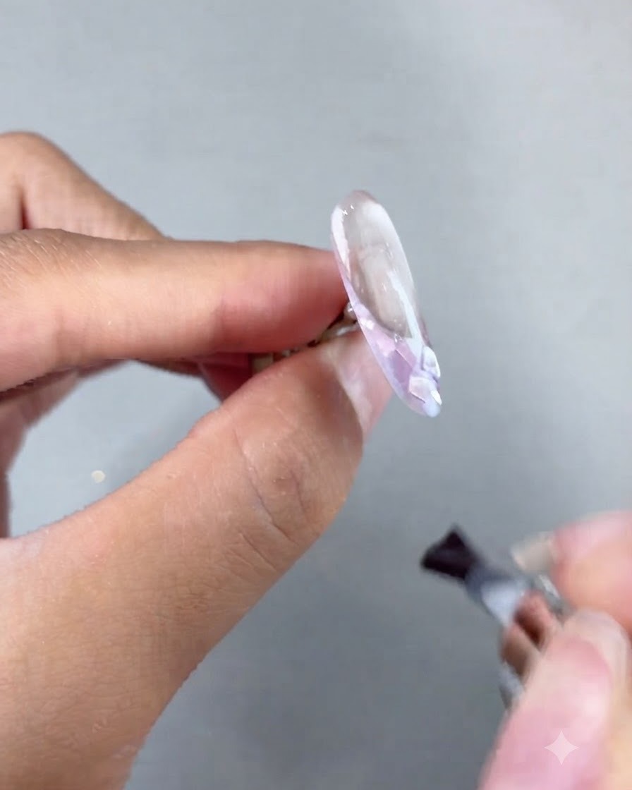 Un pincel aplicando gel constructor suave sobre una extensión de uña decorada antes del curado.