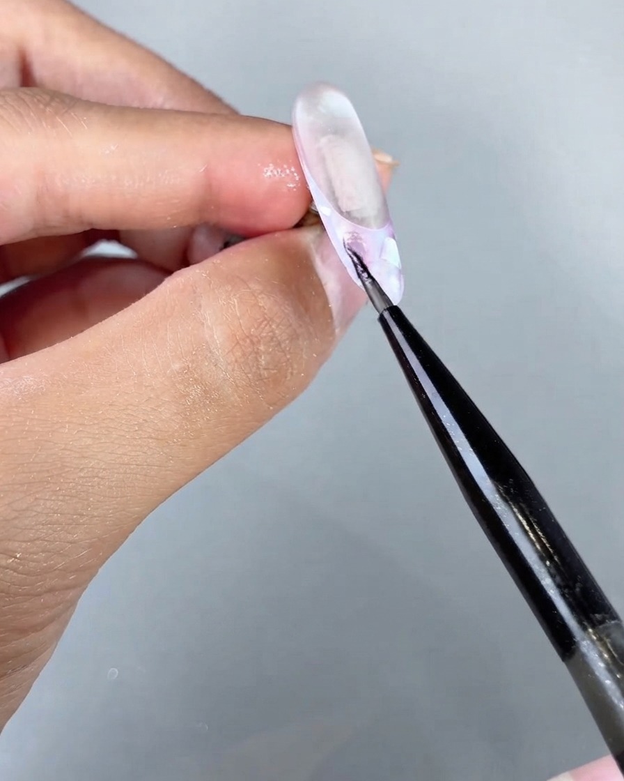 Un pincel fino aplicando gel ojo de gato mágico marino en una sección específica de un diseño de uña texturizada.