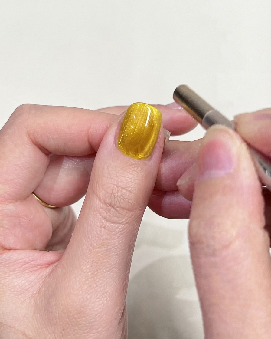 Una toma de inspección detallada de una uña de gel con ojo de gato amarillo centrada en el reflejo de luz magnética.