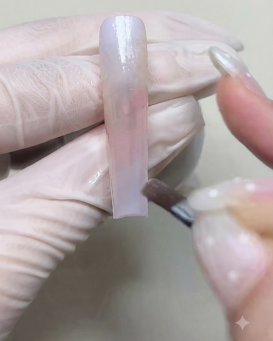 Un pincel aplicando una segunda capa de gel de color para profundizar la transición del degradado en la uña.