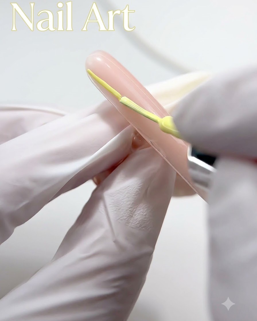 Una mano enguantada utilizando un pincel fino para aplicar esmalte en gel amarillo a lo largo de la punta de una uña de color nude.