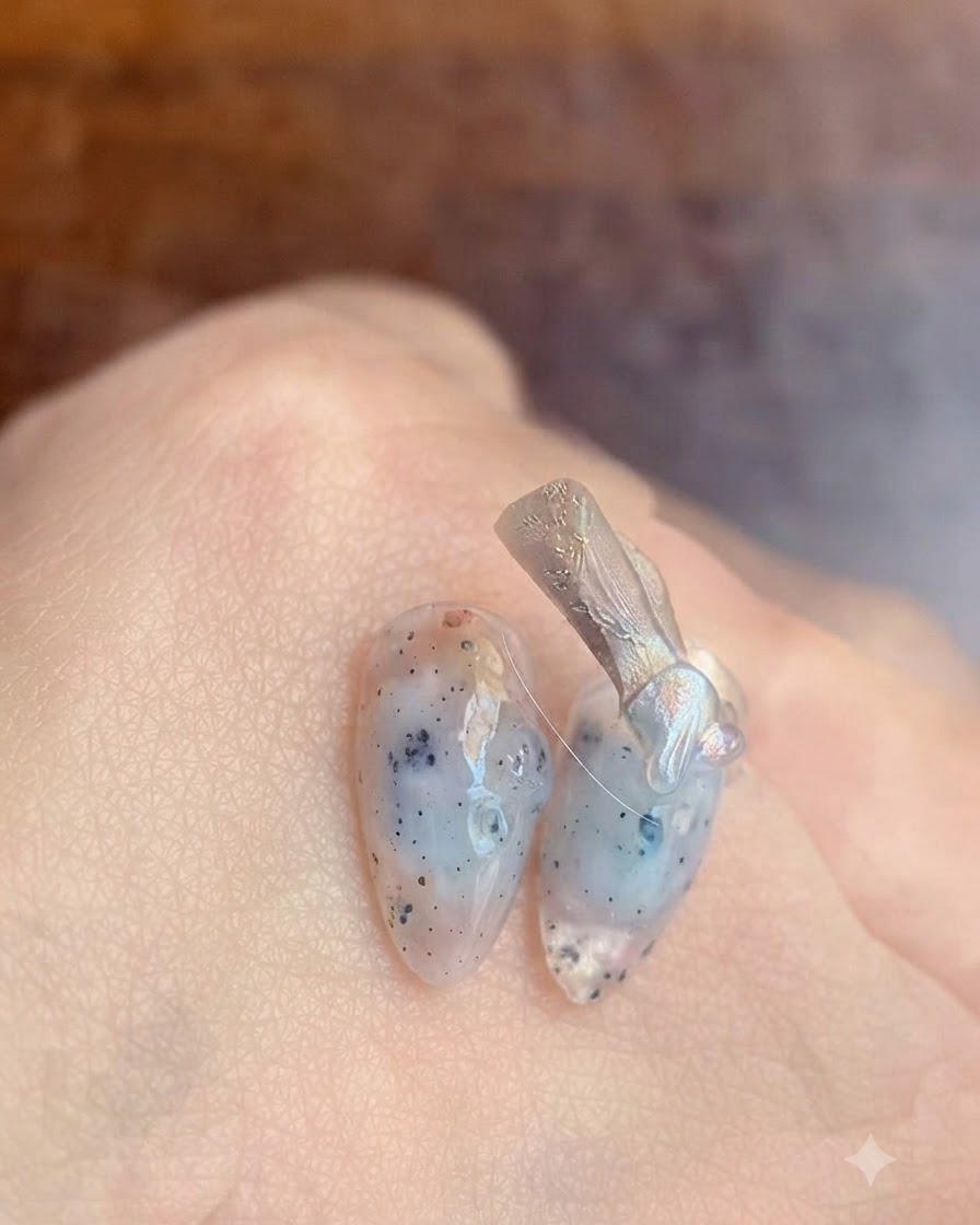 Un primer plano de un pincel de uñas aplicando una capa base de gel transparente sobre una uña natural.