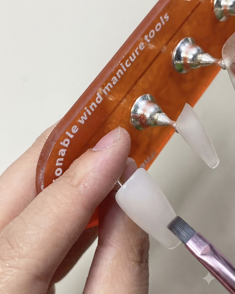 Un pincel aplicando una capa de top coat brillante sobre la extensión de uña blanca lechosa ya curada.