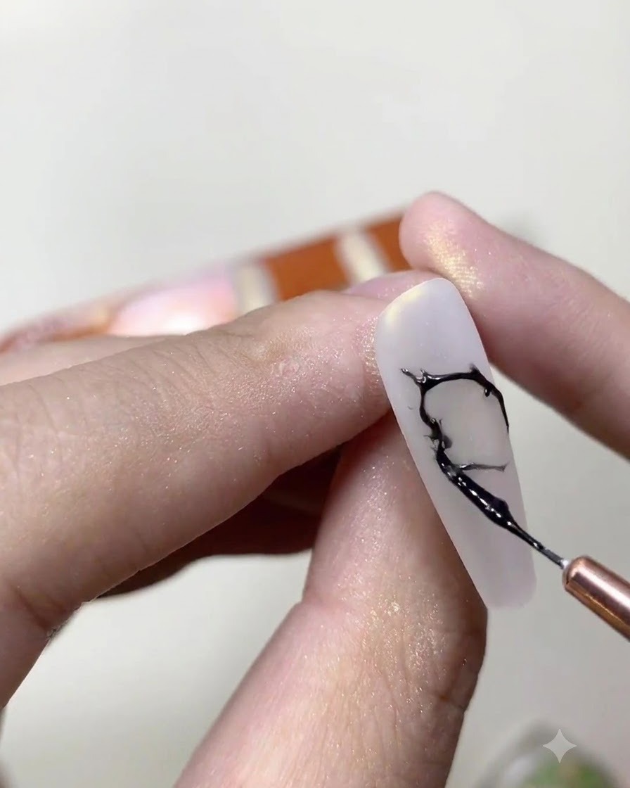 Un pincel delineador fino mezclando esmalte en gel negro y pegamento transparente para pedrería en una paleta de mezcla cosmética.