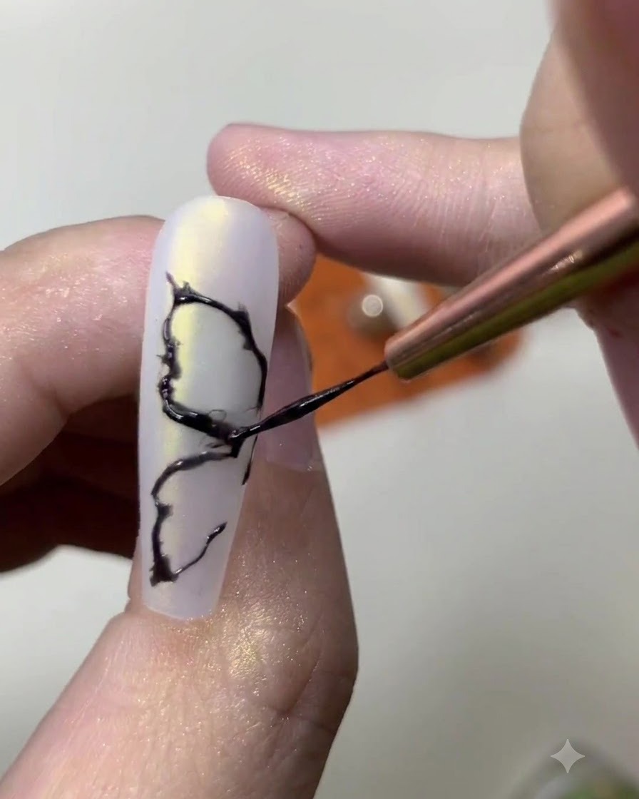 Primer plano de una manicurista agregando detalles internos finos a un diseño de ala de mariposa pintado de negro.