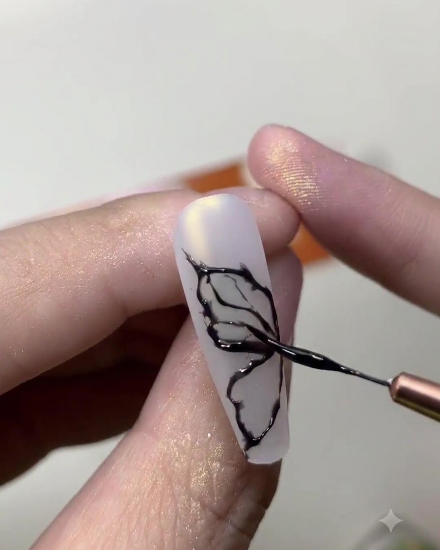 Primer plano de una manicurista usando un pincel fino para dibujar líneas delicadas de alas de mariposa negras en una uña blanco lechoso.