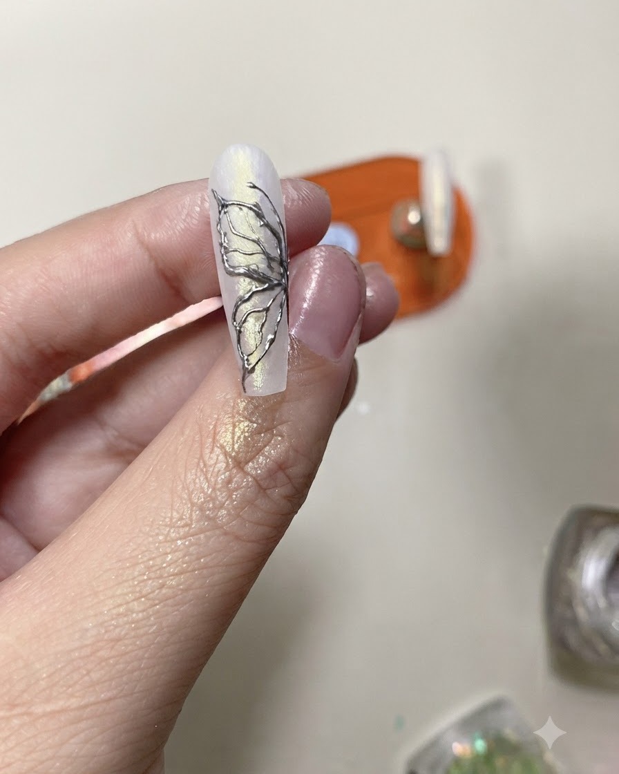 Un pincel de top coat aplicando una capa protectora transparente sobre un diseño finalizado de mariposa con cromo plateado.