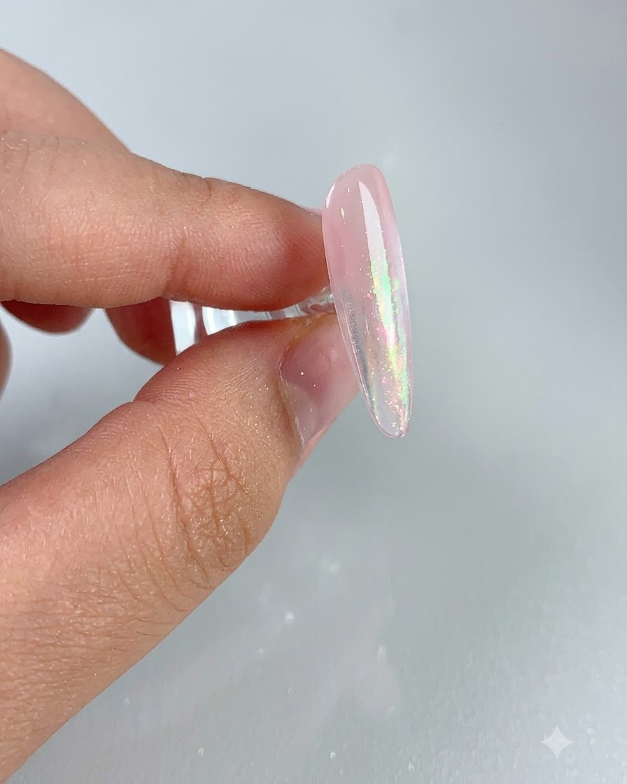 Un primer plano de una uña rosa brillante que muestra un efecto aurora brillante después de cepillar el exceso de polvo.