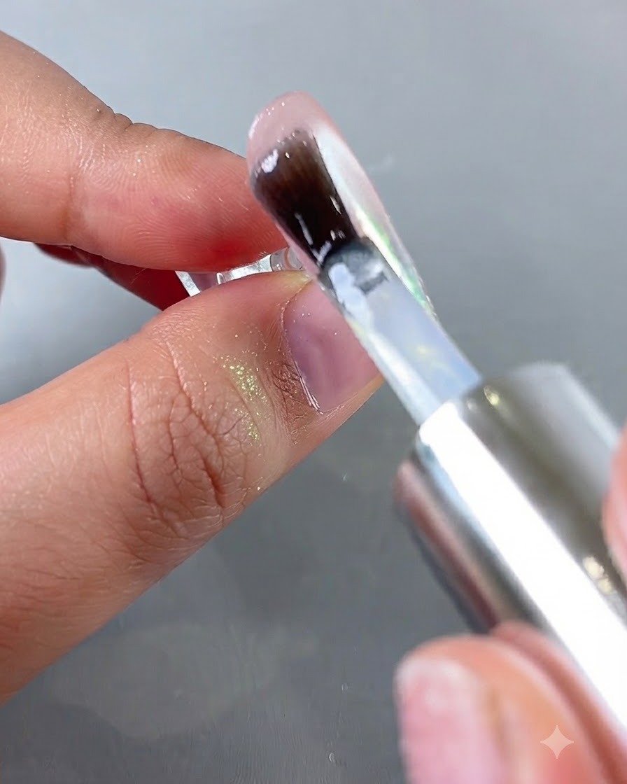 Un pincel aplicando un top coat transparente sobre la superficie brillante de una uña con cromo aurora.