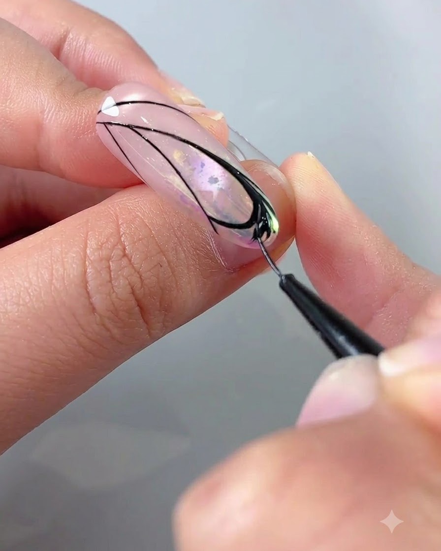 Un primer plano de una mano usando un pincel delineador con gel negro para rellenar los detalles dentro de un diseño de ala de mariposa en una uña.