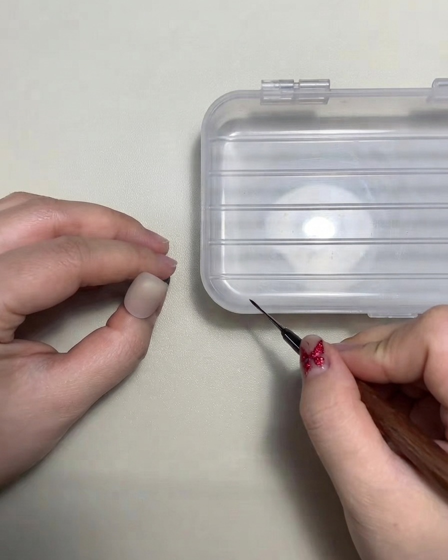 Una artista de uñas sosteniendo un pincel delineador fino cerca de la punta de una uña de práctica.