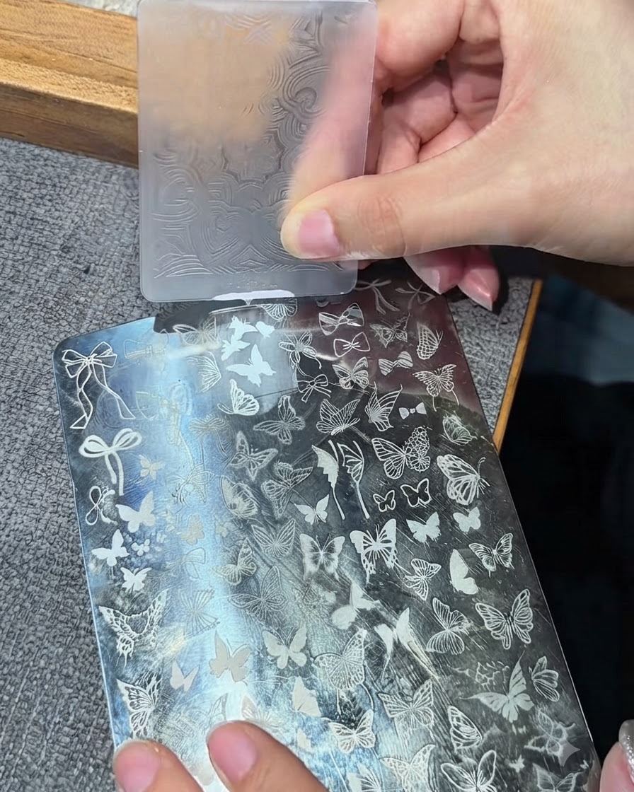 Un cabezal de estampador de silicona transparente presionando sobre una placa de estampación metálica para recoger un diseño blanco.