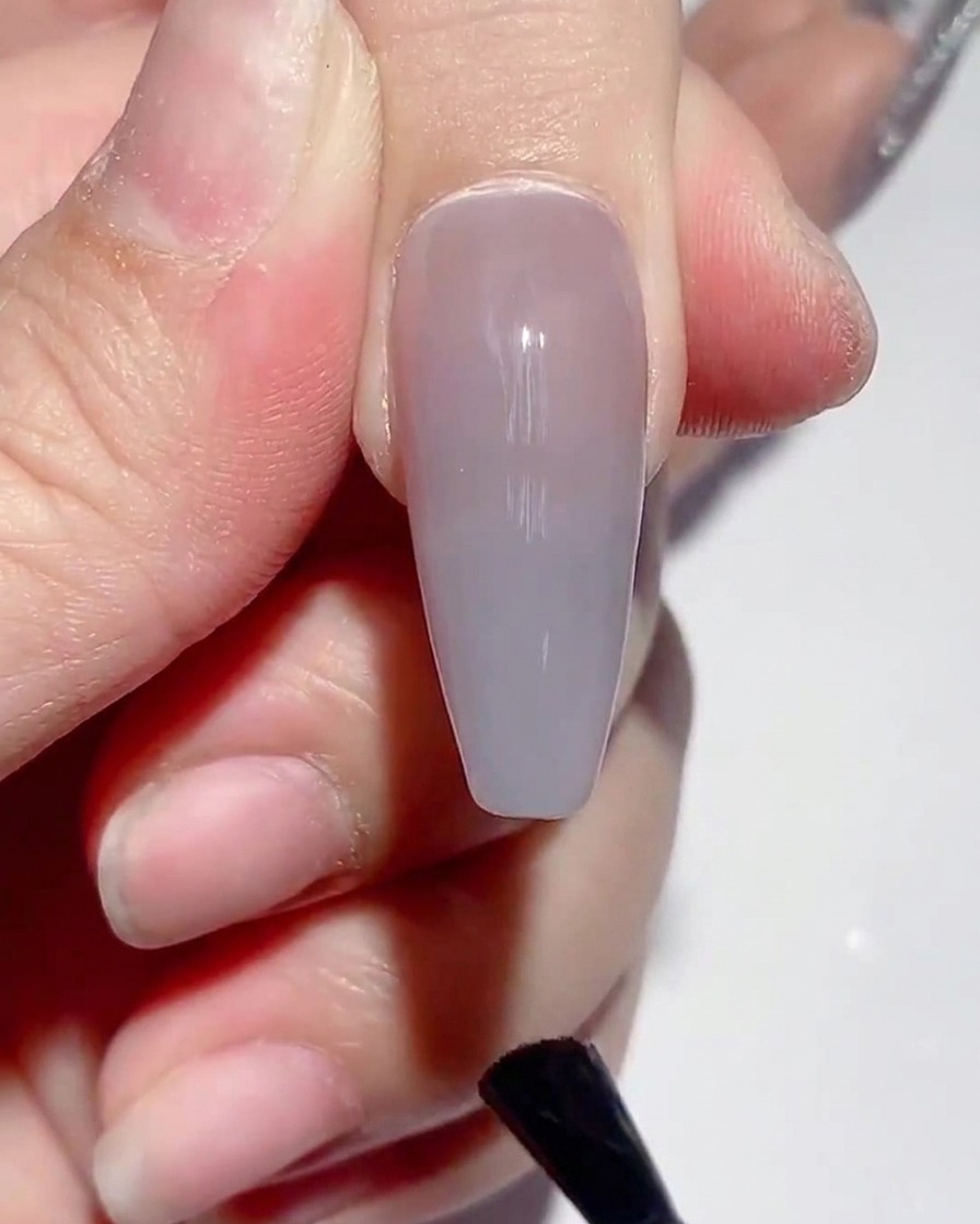 Un pincel aplicando esmalte superior mate sobre la superficie de una uña pintada.