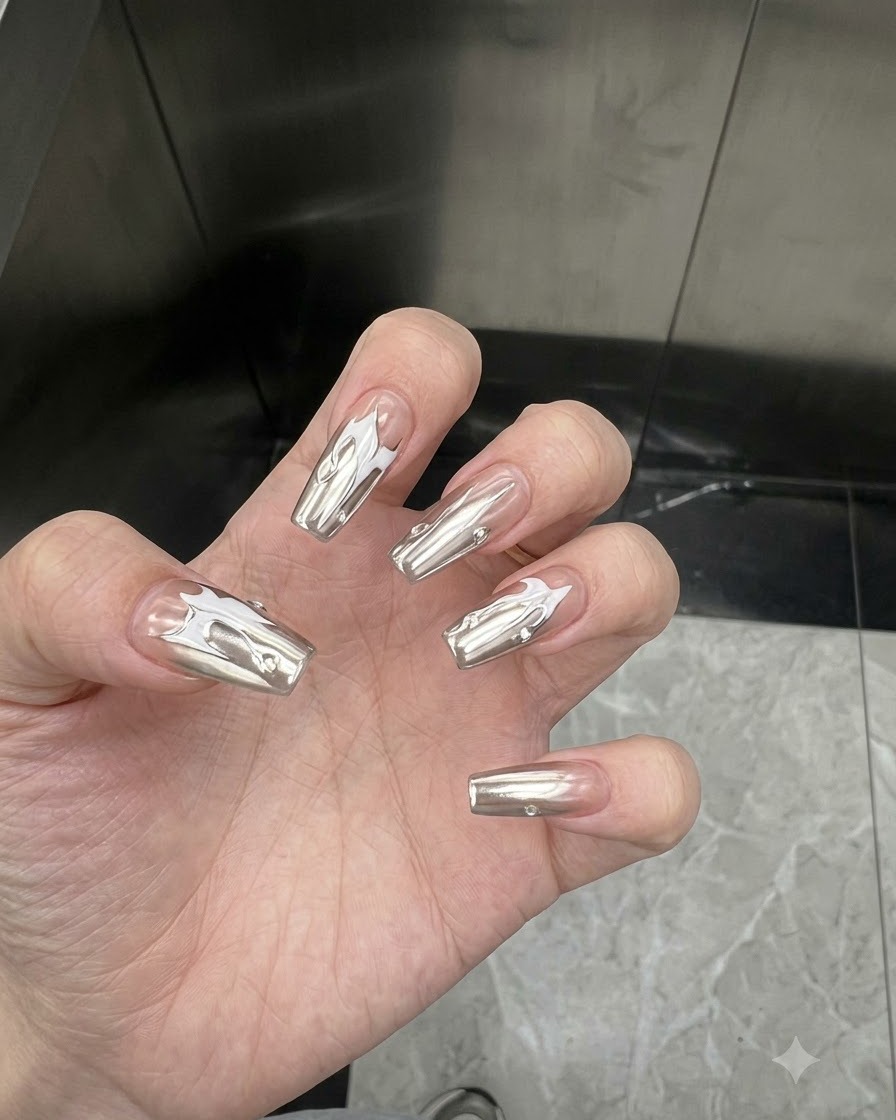 Mano inclinada para mostrar el acabado reflectante tipo espejo de las uñas con revestimiento de cromo plateado bajo iluminación interior.