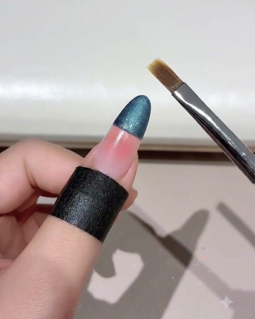 Un pincel de uñas sostenido en un ángulo cerca de una uña con degradado de ojo de gato difuminado.