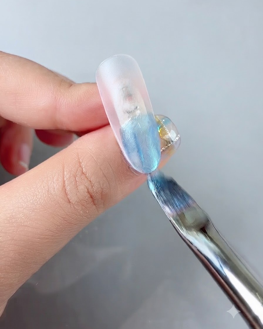 Un pincel de uñas aplicando gel de color azul vibrante en la punta de una extensión de uña transparente.