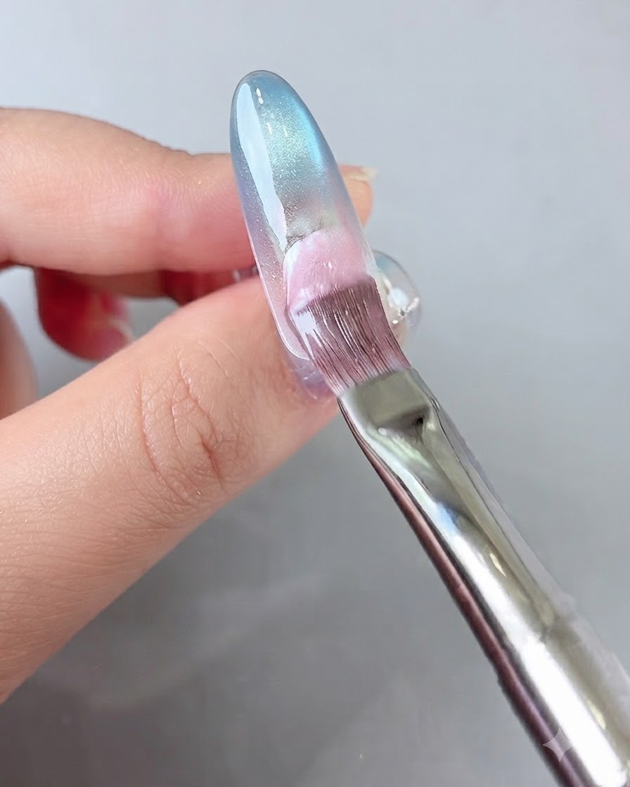 Un pincel aplicando gel rosa en la parte posterior de la uña.