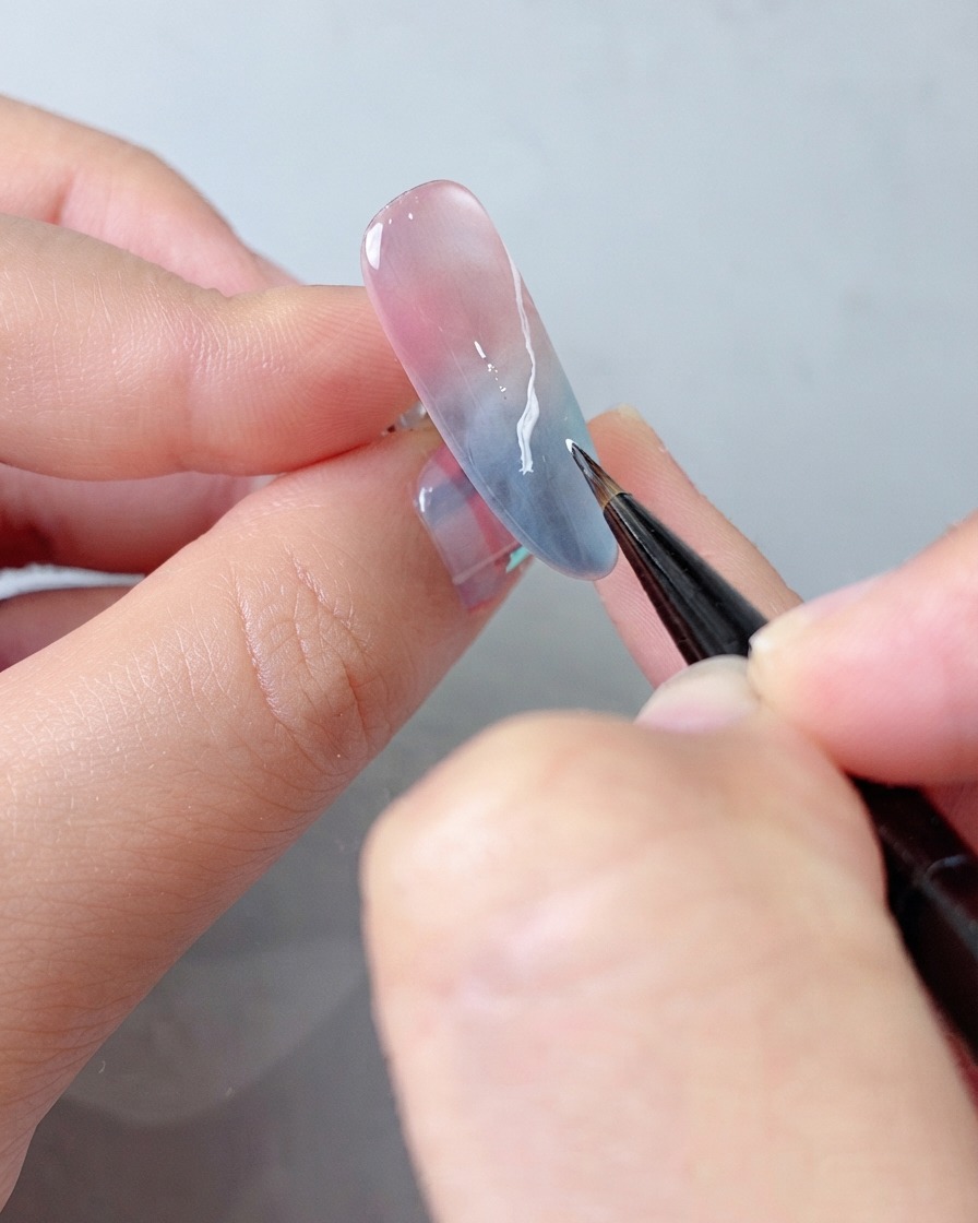 Un pincel de detalles aplicando una capa adicional de gel blanco al patrón de nubes para mejorar la profundidad.