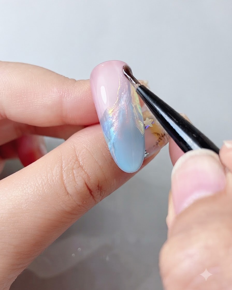 Un pincel de uñas fino aplicando un top coat transparente sobre una superficie de uña brillante y multicolor.