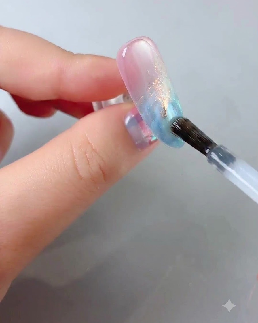 Un pincel de uñas deslizando un top coat transparente y brillante sobre la superficie de la uña decorada.