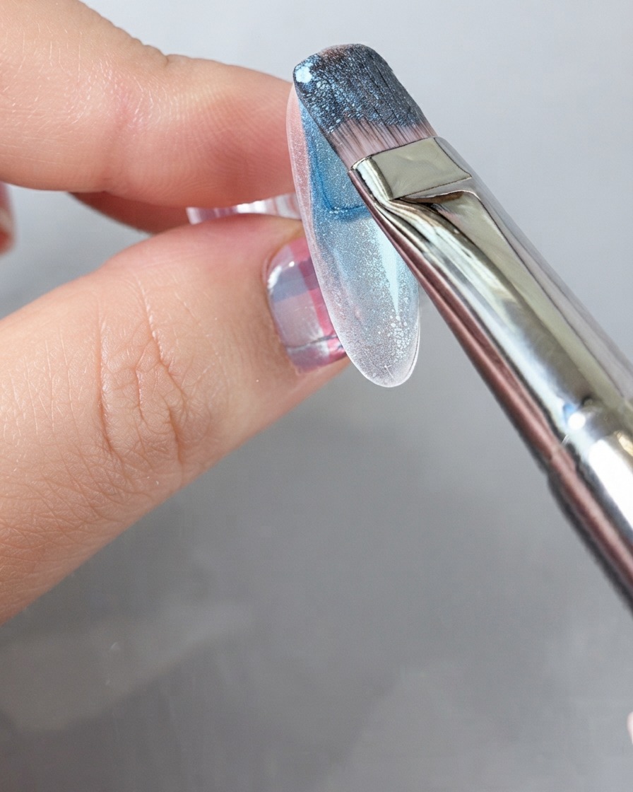 Un pincel aplicando un gel de color azul intenso en toda la superficie de una uña.