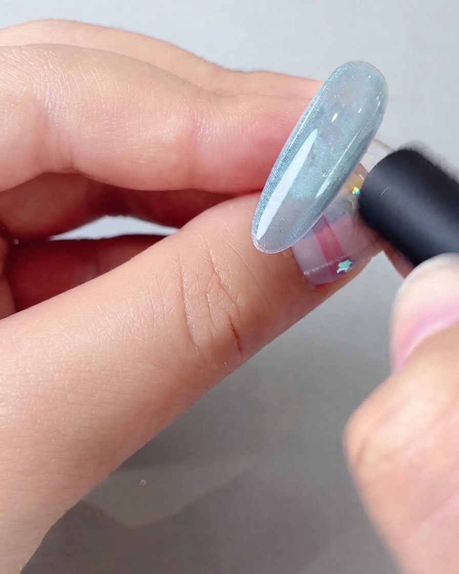 Una herramienta magnética sostenida cerca de una uña de gel azul con efecto de ojo de gato para formar un haz de luz brillante y ancho.