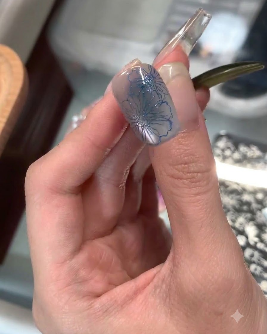 Un sello de silicona transparente aplicando un delicado estampado floral azul en la punta de una uña del dedo índice.