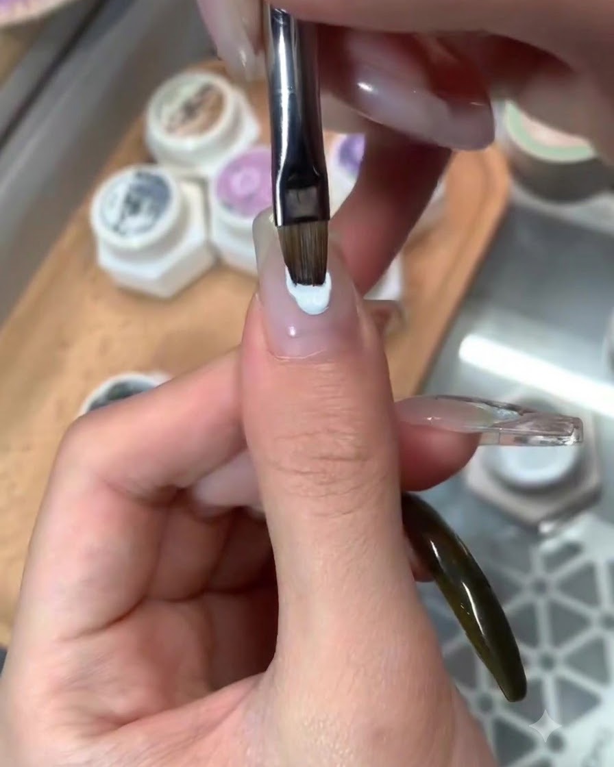 Un pincel aplicando una capa superior brillante sobre el arte de uñas con temática azul terminado.