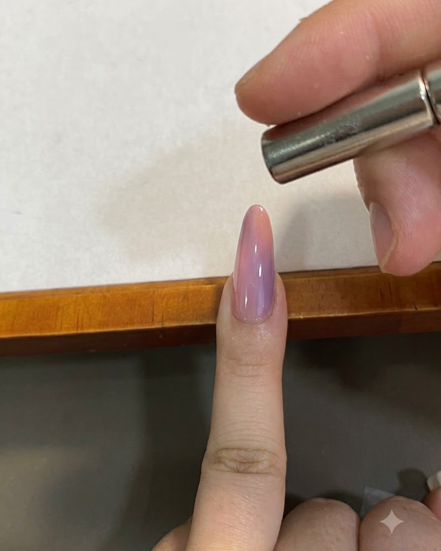 Un imán pequeño sostenido cerca y por encima de una uña cat-eye con degradado rosa para dar forma al pigmento magnético.