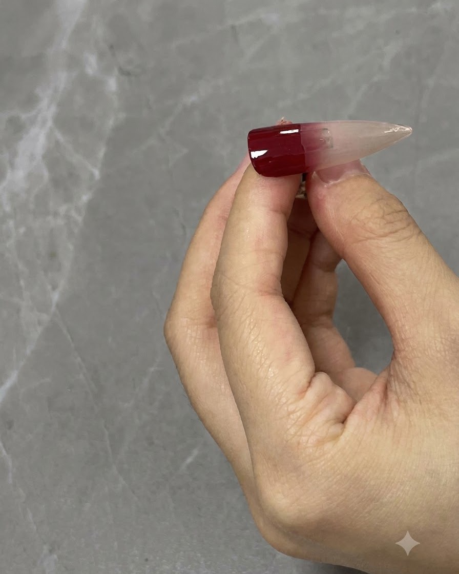 Nahaufnahme eines Nagelpinsels, der einen weinroten Farbverlauf auf einer neutralen Nagelspitze nach unten verblendet.