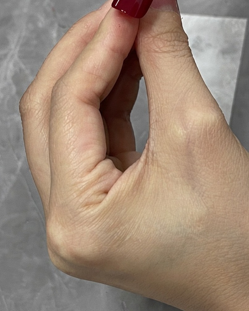 Ein Säuberungspinsel wischt überschüssiges rotes Gel um die Ränder einer Nagelspitze ab.